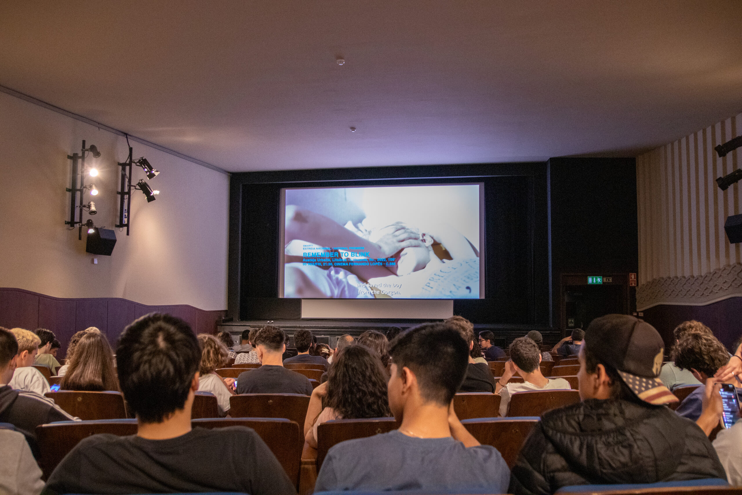 Sala de cinema com público sentado a assistir a um filme projetado num grande ecrã.